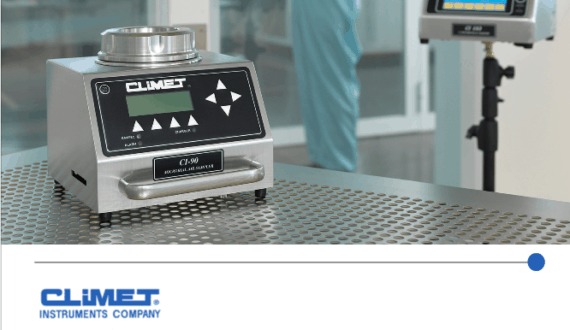 A lab worker stands by air sampling equipment in a clean, sterile laboratory environment.